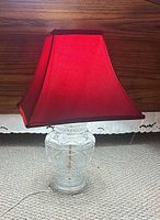 Full view of table lamp showing red shade and clear cut-glass base