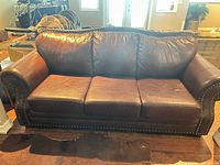 Front view of dark brown leather sofa showing three cushions and nailhead trim