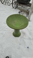 Full view of green birdbath on cylindrical pedestal in snow