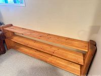 Front view of long low wooden bookcase showing three fixed shelves and honey finish