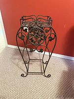 Front angle of wrought iron plant stand showing scrollwork and floral medallion
