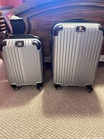 Front view of both silver suitcases showing size difference, ribbed shells, wheels, and logos