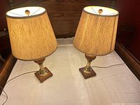 Two wood and brass table lamps on bed showing overall appearance with shades on
