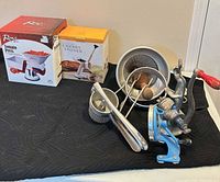 Group shot showing all canning tools, boxed Roma Tomato Press, boxed Cherry Stoner, metal grinder, strainers, food mill, jar lifter