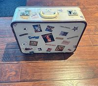 Suitcase standing upright showing front panel with stickers, handle, latches