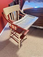 Front angled view of cream and red painted wooden high chair with metal tray attached