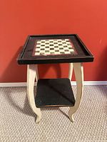 Full view of table showing checkerboard top, cream legs, black shelf