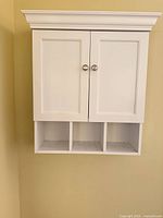Front view of white wall-mounted cabinet showing doors closed and three cubbies