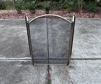 Front view of three-panel brass-tone arched fireplace screen on pavement