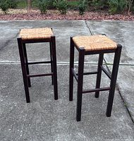 Pair of tall backless barstools with wood frames and woven rush seats outdoors