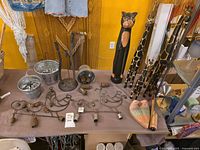 overview of table showing carved cat, giraffes, galvanized pails with metal rods, wire chickens with bells, carved heart, loose metal hardware