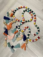 Two colourful wool felt ball garlands with tassels displayed coiled on floor
