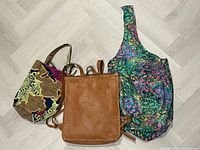 Front view of three bags: brown leather backpack, multicolour sling tote, yellow geometric tote