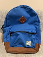 Front view of royal blue Herschel backpack showing main body, front pocket, brown base and side mesh pocket