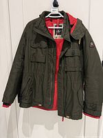 Full view of olive jacket with red lining on hanger