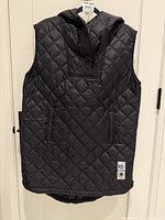 Front view of black quilted hooded extra-long vest on hanger