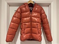 Front view of orange Save The Duck puffer jacket hanging on hanger