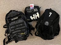 All three bags side by side: WOLFpak camo backpack, folded Helly Hansen 30 L duffel, Etobicoke FC backpack