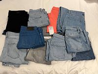 All eleven pairs of jeans spread on bed showing colors and pocket styles