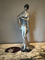 Full view of silver-toned geisha statue on base with brand plaque nearby