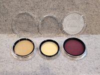 Three lens filters in cases, lids open, showing filter surfaces