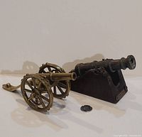 Both brass cannons side by side with coin for scale