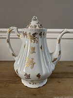 Full view of white porcelain teapot with gold decoration and lid