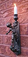 Front view of brass cherub wall sconce holding lit candle