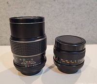 Both lenses upright, 135 mm on left, smaller 2.8 lens on right with caps