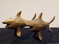 Front left perspective of both brass shark figurines showing open mouths and fins