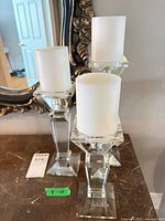 Three clear glass candlesticks with white pillar candles on dark surface