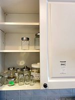 Cabinet shelf showing multiple small spice jars, cookie canister, cruet and other glass pieces