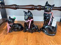 All three black ceramic cat figurines side by side showing relative sizes and pink ribbons
