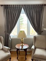 Curtains installed on window with tie backs, chairs and lamp for scale