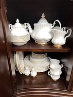 teapot, covered sugar bowl, creamer, plates and cups on cabinet shelves