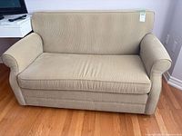 Front view of beige loveseat sofa bed showing single cushion and rounded arms