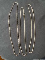 Three sterling silver chains laid flat on dark cloth