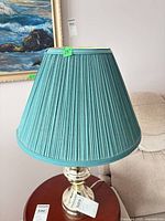 Full view of one lamp showing teal pleated shade and brass-tone base