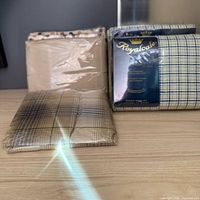 Assorted packaged sheet sets and flat sheets on surface, showing Royalcale blue/cream check, Martex plaid, Martex polka dot and others