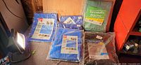 Five tarps in wrappers: three blue, one green, one black