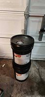 Two stacked black 5-gallon pails of hydraulic oil