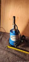 Front view of blue Powerfist submersible pump with cord and discharge pipe, tape measure indicates size