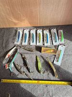 All lures laid out: eight sealed on cards, nine loose below with measuring tape for scale