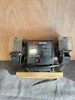 Front view of bench grinder showing wheels, base, eye shields and power cord