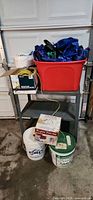 Shelving unit with red tote of tarps, bucket and boxes of rope, twine and cords