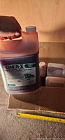 Hand holding labeled Chain-X 3.7 L oil jug above box