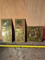 All three brass-tone wall plaques with measuring tape for scale