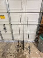 Three fishing rods with reels leaning against garage door