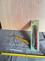 Overview showing yellow folding saw open, packaged red folding saw, spare blade and tape measure for scale