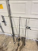 Three fishing rods with reels leaning against garage door